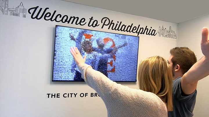 A couple adding themselves into a mirror photo mosaic on a tv screen